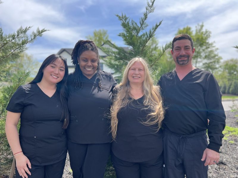 Four dental assistants members, three women and one man, posing together outdoors in black medical scrubs.